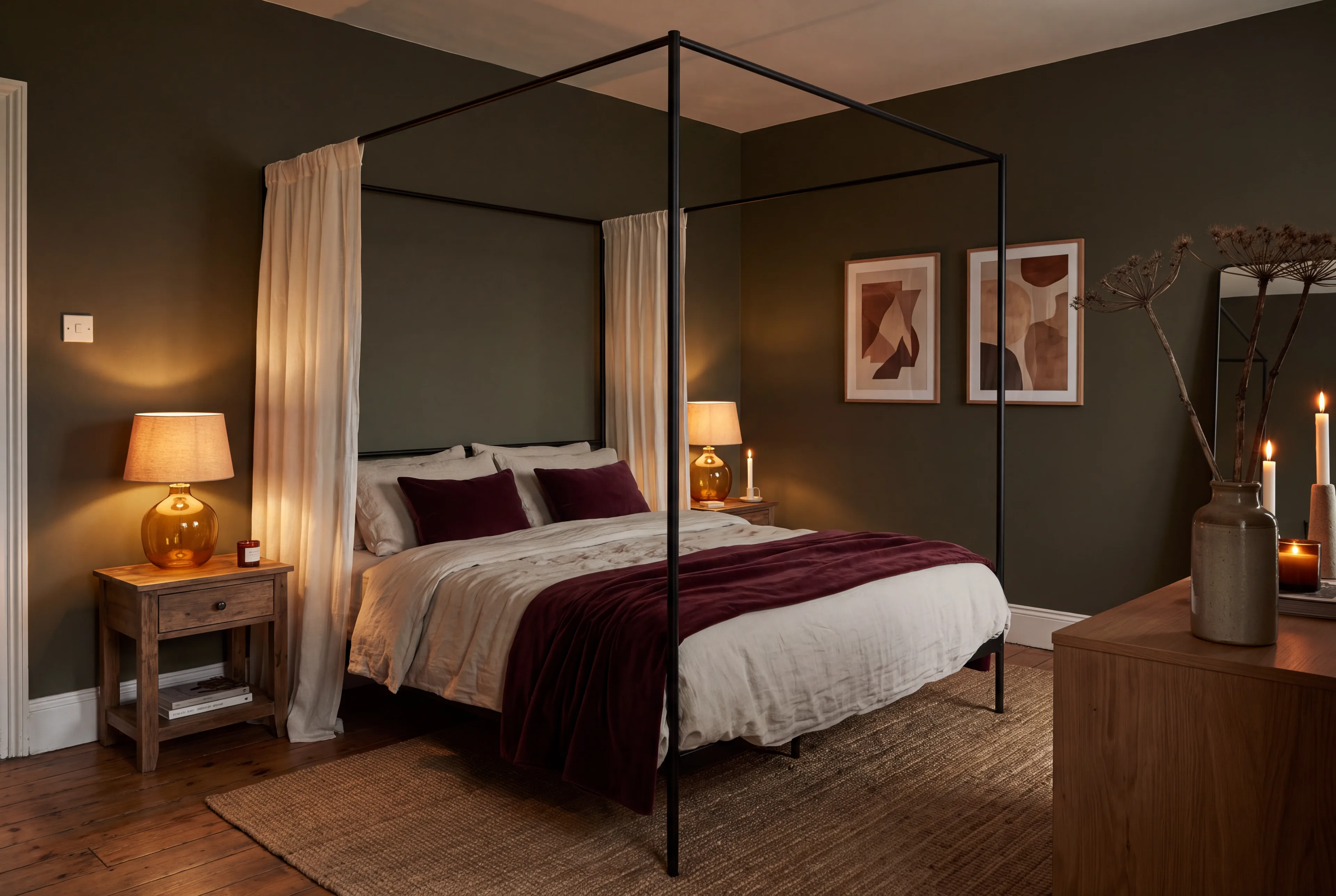 An olive-green bedroom with a slim black canopy bed, linen bedding, a wine velvet throw and amber lamps